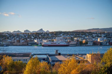 Tromso, Norveç 'in arka planında güz yapraklarıyla çevrili büyük Hurtigruten feribotu ve dağları olan bir nehir manzarası.