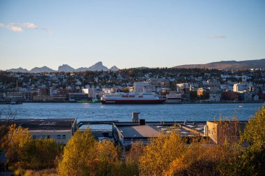 Tromso, Norveç 'in arka planında güz yapraklarıyla çevrili büyük Hurtigruten feribotu ve dağları olan bir nehir manzarası.