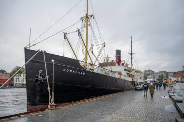Rogaland adında büyük siyah bir gemi Stavanger rıhtımına yanaştı. Norveç 'te kaldırım taşları üzerinde turistler yürüyor.