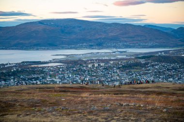 Storsteinen, Tromso, Norveç 'ten, şehrin panoramik manzarası yuvarlanan tepeler ve büyük bir su kütlesi arasında toplanmış, insanlar bir tepenin üzerinde toplanmış.
