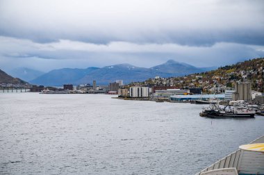 Tromso, Norveç, endüstriyel binalar ve teknelerle dolu bir liman, bulutlu bir gökyüzünün altında dağlık bir zemin üzerine kurulmuş.