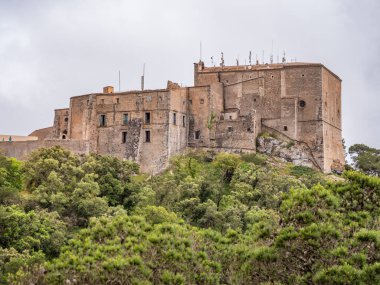 Santuari de Sant Salvador, Mallorca, tarihi taş kale, yemyeşil bir tepenin yamacında, görkemli bir şekilde bulutlu bir gökyüzü altında duruyor, Majorca.