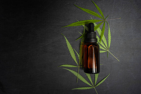 Вид сверху на бутылку с маслом и листья на черном фоне.