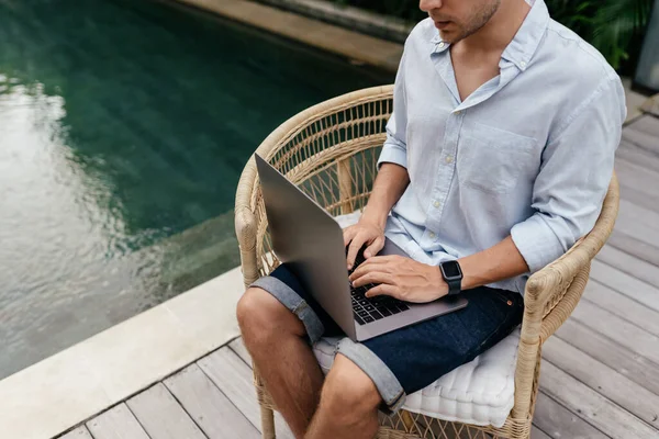 Νεαρός που χρησιμοποιεί φορητό υπολογιστή σε κήπο με πισίνα. — Φωτογραφία Αρχείου