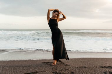 Kumsaldaki kadın, tatil boyunca sakin okyanus doğasının tadını çıkarıyor.