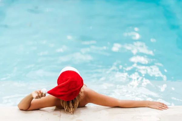 Ung kvinna i julen hatt och baddräkt firar nyår vid poolen. — Stockfoto