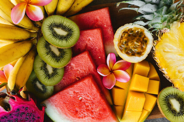 Tropical fruits assortment on a wooden plate. Stone background.