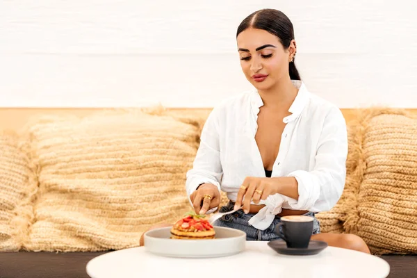 Mooie jonge vrouw die pannenkoeken eet in een café — Stockfoto