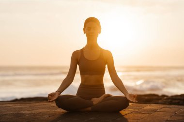 Sahilde gün batımında yoga. Kadın asanas gösterisi yapıyor ve okyanustaki hayatın tadını çıkarıyor.