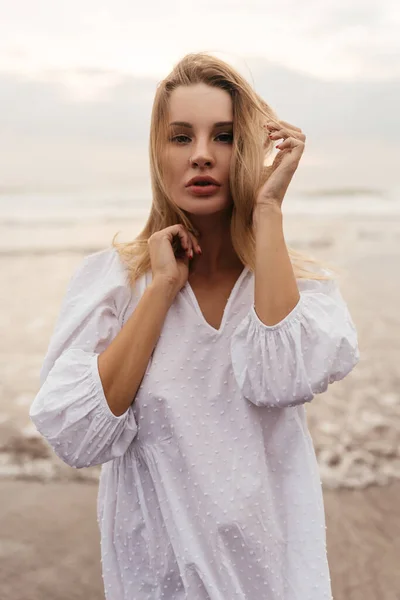 Jonge vrouw draagt mooie witte jurk loopt op het strand tijdens zonsondergang — Stockfoto