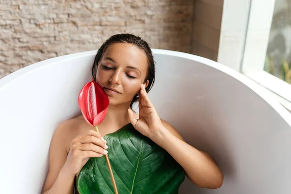 Retrato de uma jovem mulher com flor de antúrio deitada em banho trópico. — Fotografia de Stock