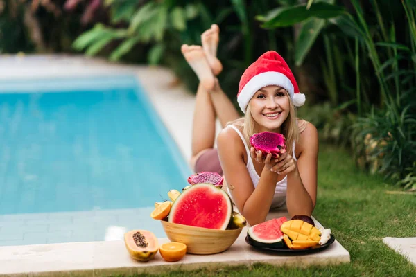 Jul kvinna vacker leende i tomte hatt med en tropisk frukt — Stockfoto