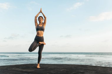 Okyanus manzaralı doğada yoga yapan genç bir kadın..