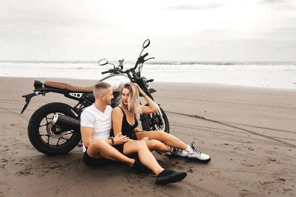 Unga par ryttare tillsammans på sandstrand med motorcykel — Stockfoto