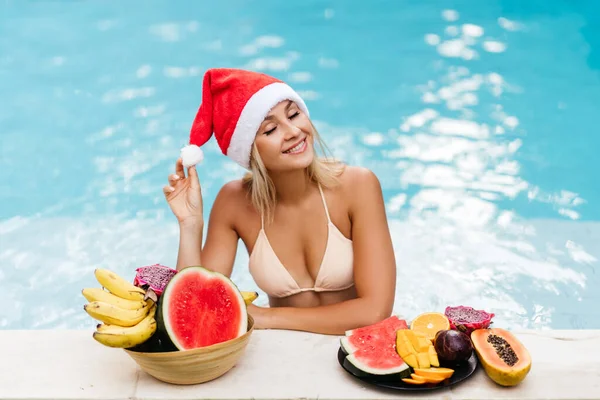 Weihnachtsfrau schön lächelnd in Santas Hut mit tropischen Früchten — Stockfoto
