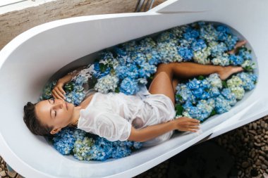 Banyoda tropikal mavi ortancayla dinlenen bir kadın..