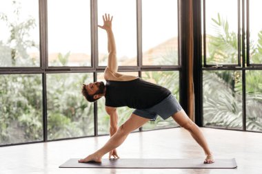 Yogacı adamlar stüdyoda pencerenin önünde egzersiz yapıyor.