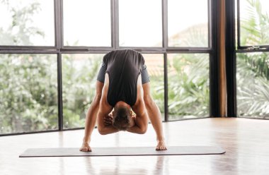 Yogacı adamlar stüdyoda pencerenin önünde egzersiz yapıyor.