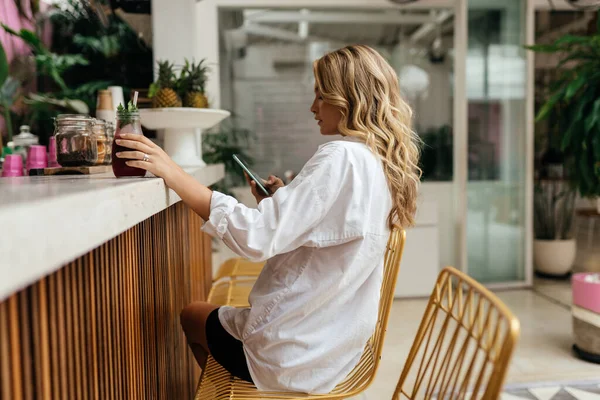 Elegante mujer delgada iin café, mientras que los mensajes de texto en el teléfono inteligente y beber jugo de refrigeración — Foto de Stock