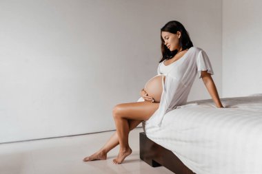 Güzel hamile kız yatakta oturuyor.