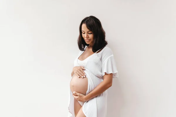 Těhotná žena drží ruce na břiše na bílém pozadí. — Stock fotografie