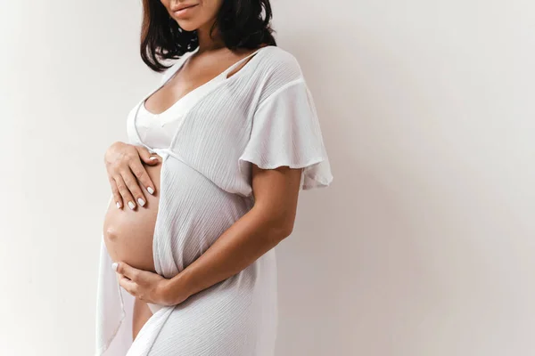 Donna incinta si tiene per mano sulla pancia su uno sfondo bianco. — Foto Stock