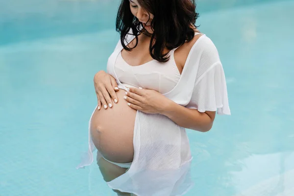 Donna incinta rilassarsi a bordo piscina e toccare la pancia con le mani — Foto Stock