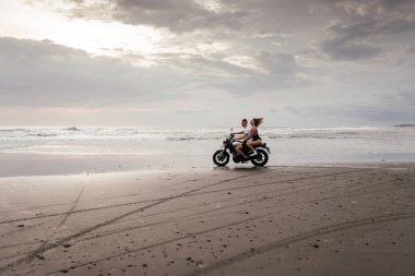 Kumsalda motosiklet süren genç bir çift.