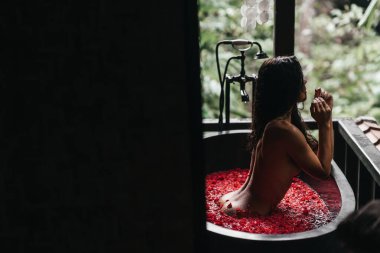 Küvette gül yapraklı güzel bir kadın. Vücut bakımı.