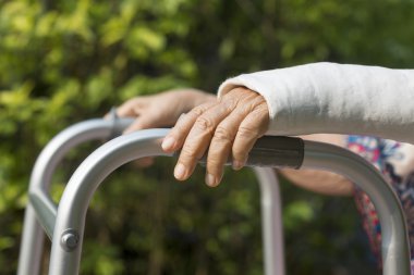 kadın kıdemli kırık bilek Walker arka bahçesinde kullanarak.