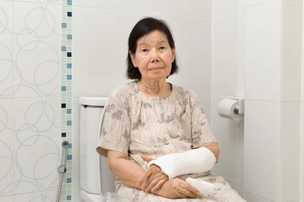 Mujeres mayores brazo roto en yeso usando el inodoro . — Foto de Stock