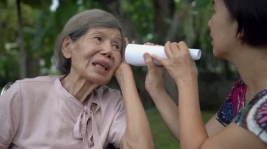 Kız, kağıt tüp kullanarak işitme engelli yaşlı bir kadınla konuşuyor.