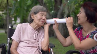 Kız, kağıt tüp kullanarak işitme engelli yaşlı bir kadınla konuşuyor.