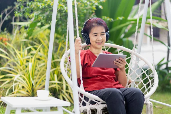 中年女性リラックスオンスイングリッスン音楽オンザタブレットコンピュータ上の裏庭 — ストック写真