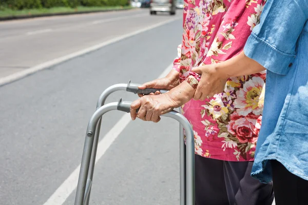 Äldre kvinna med en rullator cross street — Stockfoto