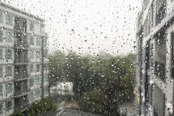Regentropfen auf einer Fensterscheibe, Gebäude im Hintergrund. — Stockfoto