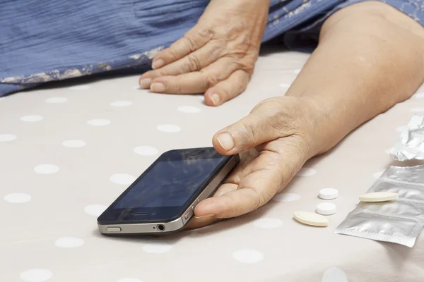 Äldre kvinna sova i sängen och hålla en mobiltelefon. — Stockfoto