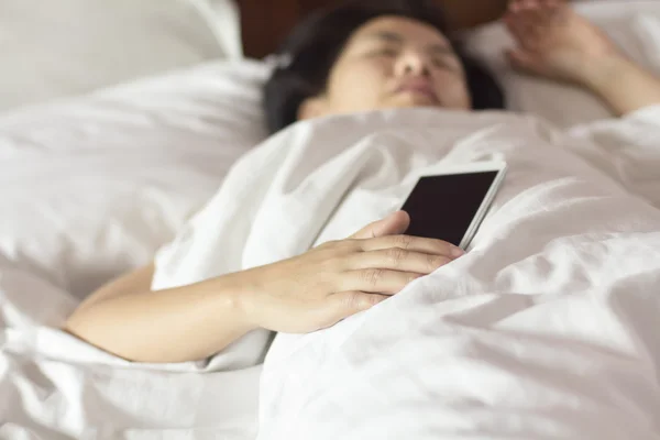 Женщина спит в постели и держит мобильный телефон. — стоковое фото