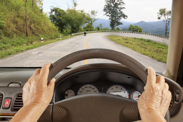 Mujer mayor conduciendo un coche en carretera de montaña . — Foto de Stock