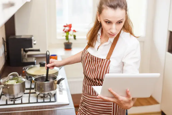 Jeune femme qui tente de cuisiner avec la recette de l’ordinateur portable Images De Stock Libres De Droits