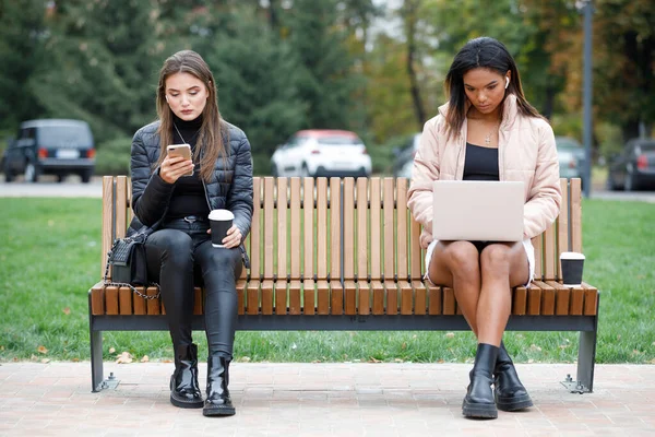 Two different women sitting on the bench in park — Stock Photo, Image