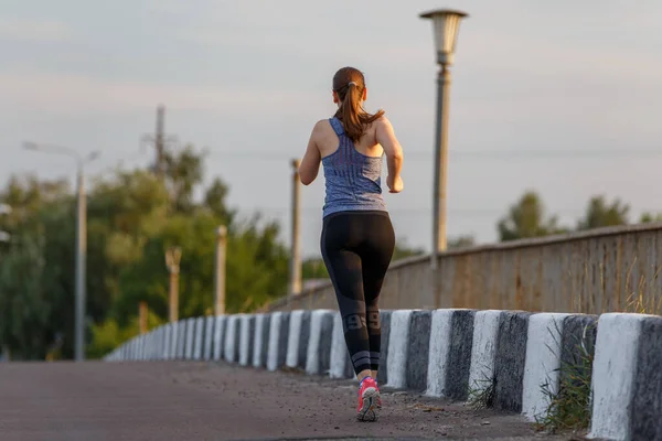 Вид сзади на бегущую молодую женщину на дороге — стоковое фото