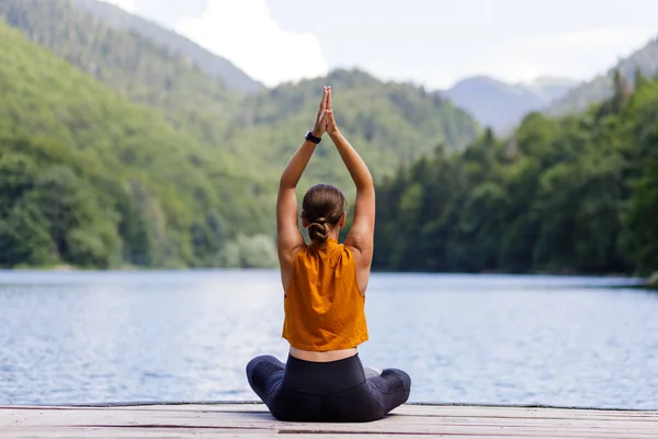 Fiatal nő meditál vagy jógázik a tónál a hegyekben — Stock Fotó