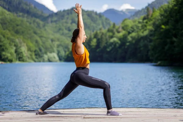 Young woman doing warrior yoga pose near the lake