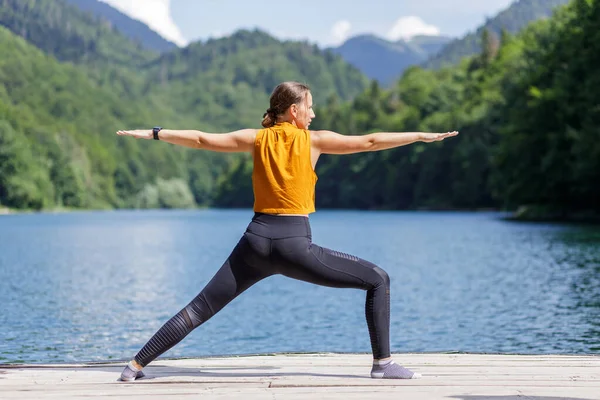 Junge Frau posiert in der Nähe des Sees beim Krieger-Yoga — Stockfoto