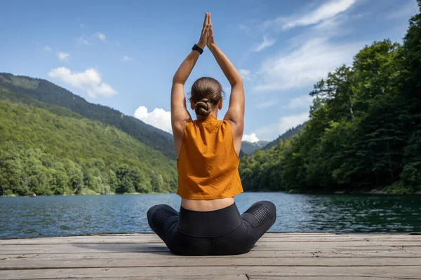 Junge Frau meditiert oder praktiziert Yoga am See in den Bergen — Stockfoto