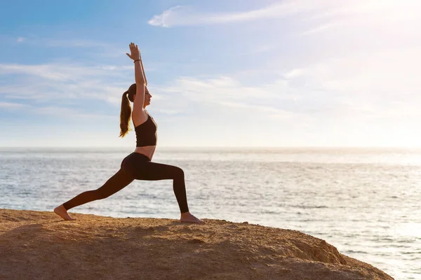 Young fitness woman practicing yoga at the seashore in the morning — Stock Photo, Image