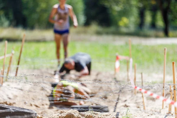 Gli sportivi strisciano sotto l'ostacolo del filo spinato sul loro percorso in corsa ad ostacoli — Foto Stock