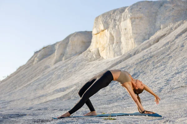 Giovane donna che pratica yoga a scogliere bianche al mattino. Cosa selvaggia posa yoga contro il tramonto Foto Stock Royalty Free