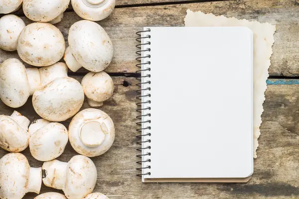 Cogumelos com livro de culinária em branco ou folha de receita sobre fundo de madeira — Fotografia de Stock